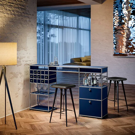 Eine Bar aus stahlblauem USM Haller steht frei im Raum. Zwei Barhocker dienen als Sitzmöglichkeit.